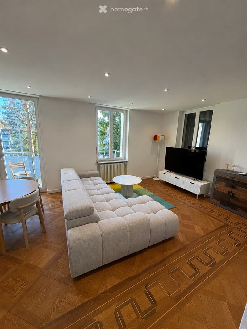 Modern living room with a sectional sofa, coffee table, dining area with chairs and table, television on a stand, and a floor lamp near the window.