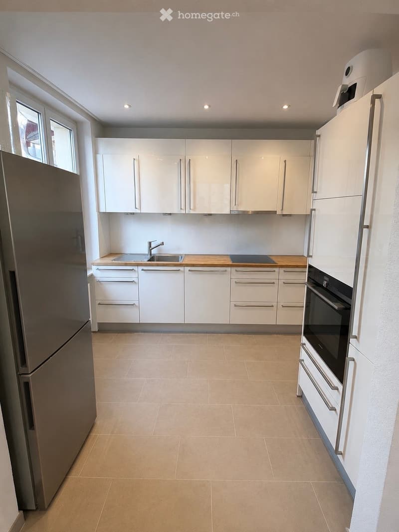 Modern kitchen with white cabinets, stainless steel appliances, and a wooden countertop.