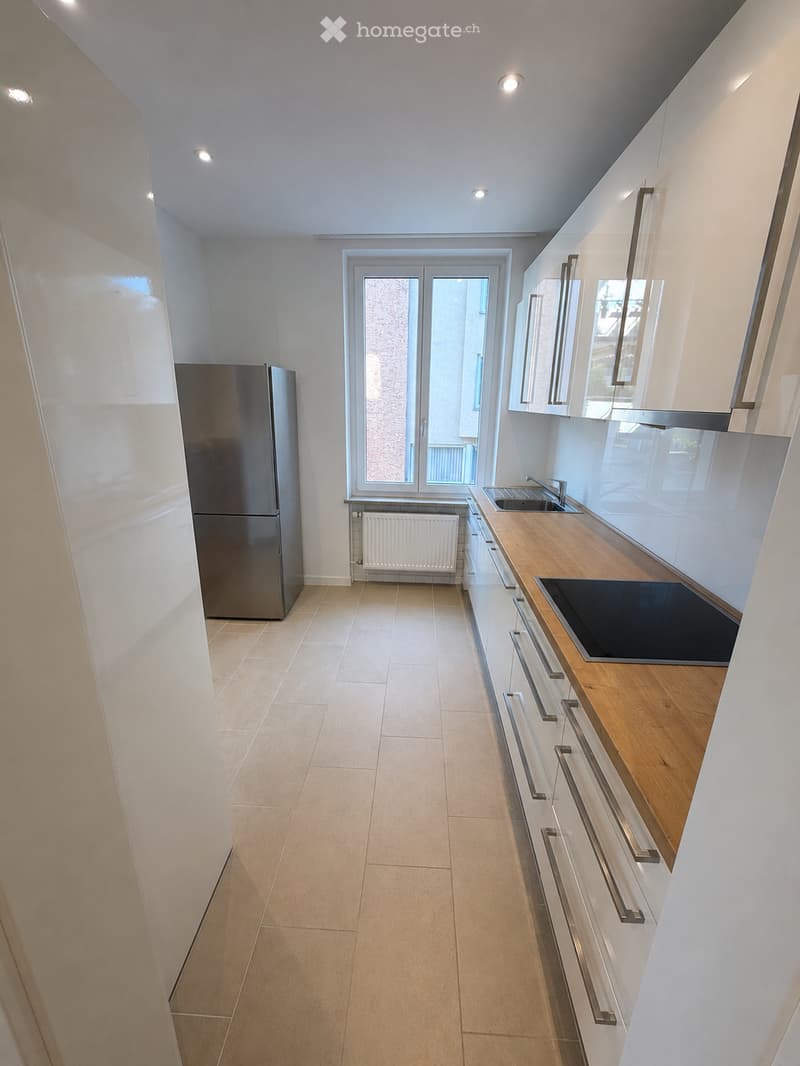 Modern kitchen with white cabinets, wooden countertop, stainless steel appliances, and large window with double doors leading outside.