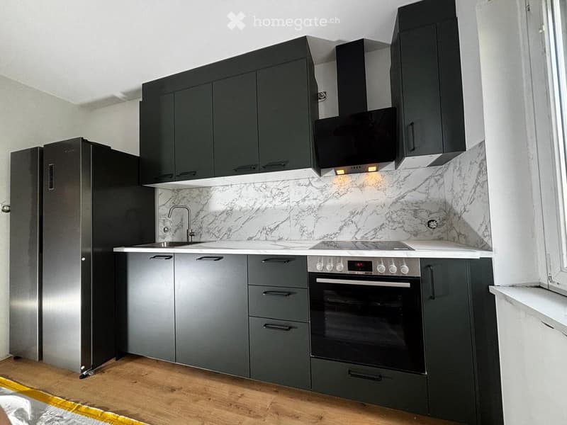 Modern kitchen with dark grey cabinets, marble backsplash, stainless steel appliances, and wooden flooring.