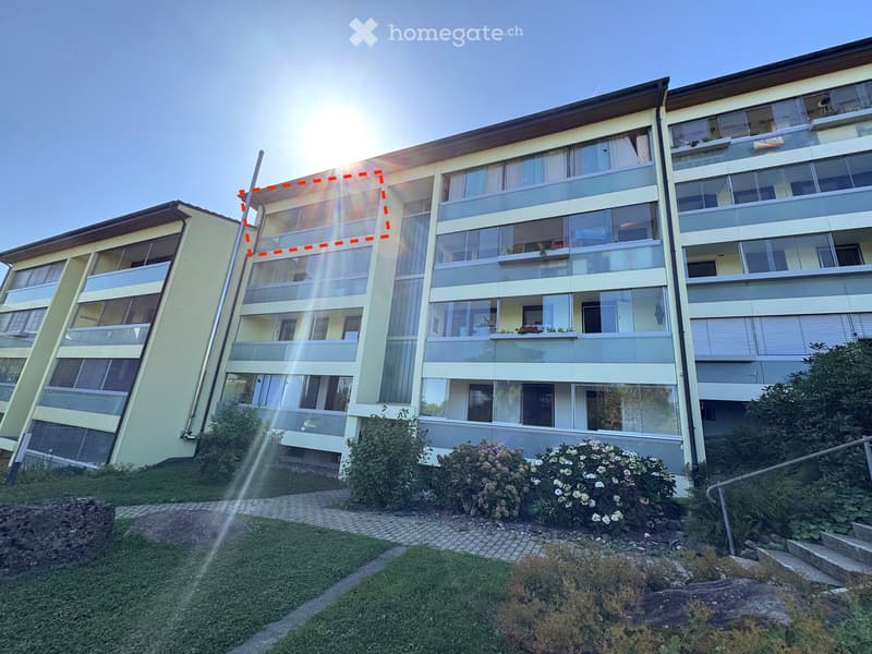 Modern multi-story residential building with large windows, balconies, and surrounding greenery.