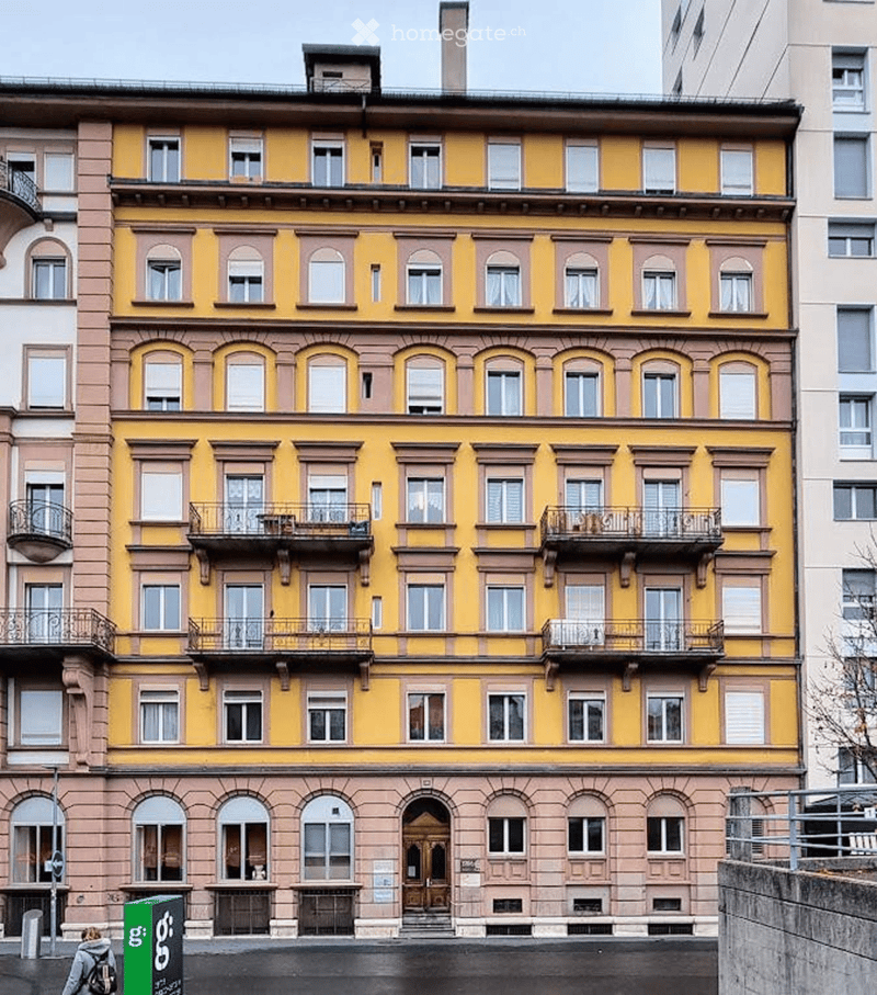 A multi-story residential building with yellow and pink facade, multiple windows, balconies, and ornate architectural details.