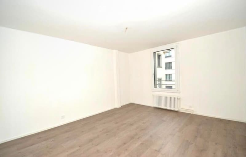 Empty room with white walls, wooden flooring, and a single window with a radiator below it.