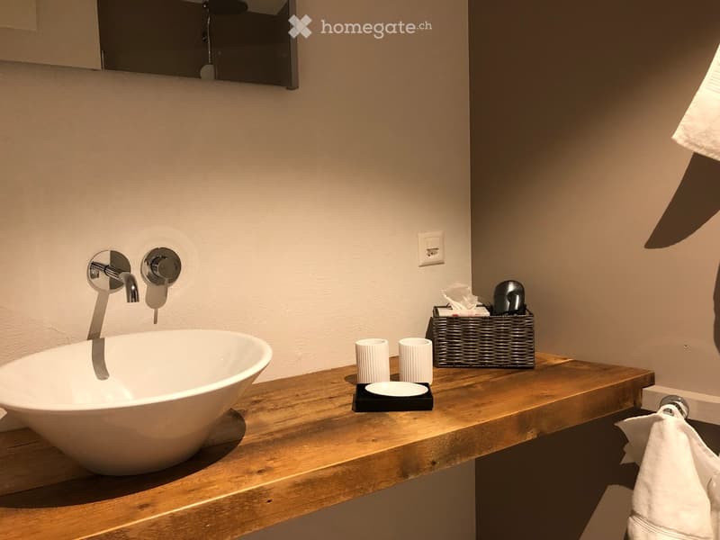 Modern bathroom with a wooden countertop, white sink bowl, sleek faucet, and a wicker basket holding toiletries.