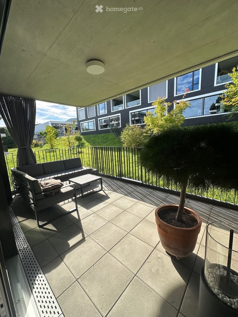 outdoor seating area with couch and table, metal railing, black curtain, potted tree, decorative pebbles