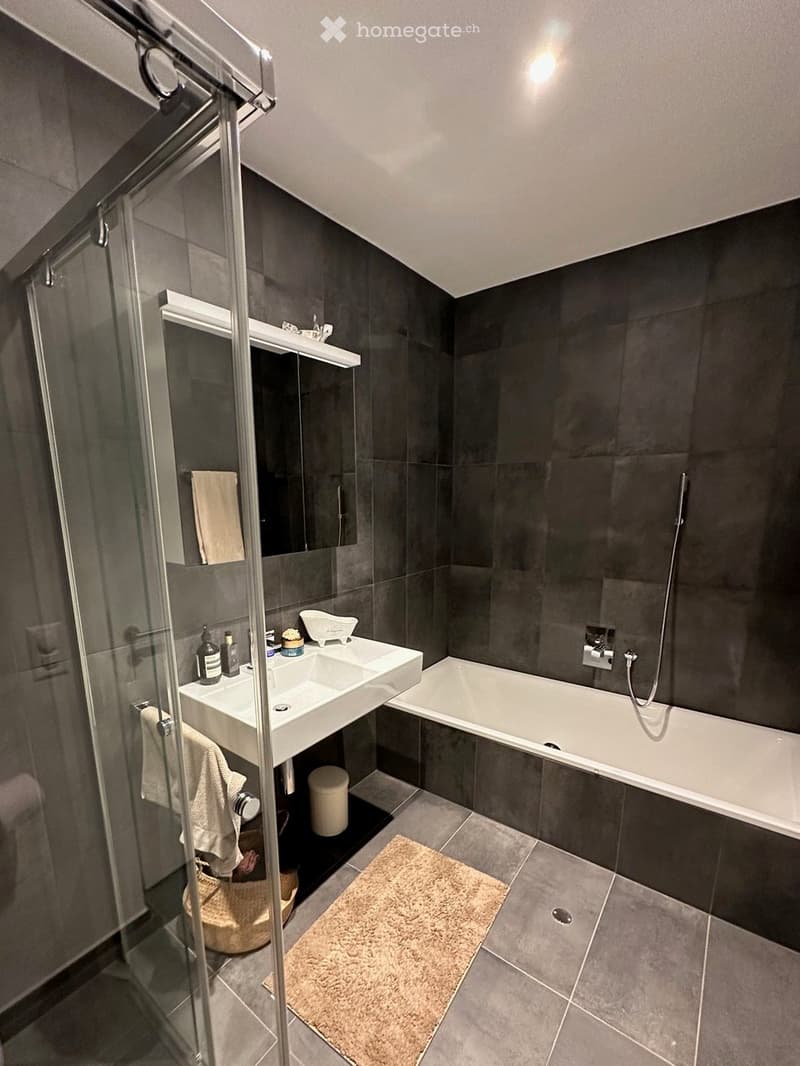 modern bathroom with a glass shower enclosure, white bathtub, white sink with mirror, towels, and a beige rug