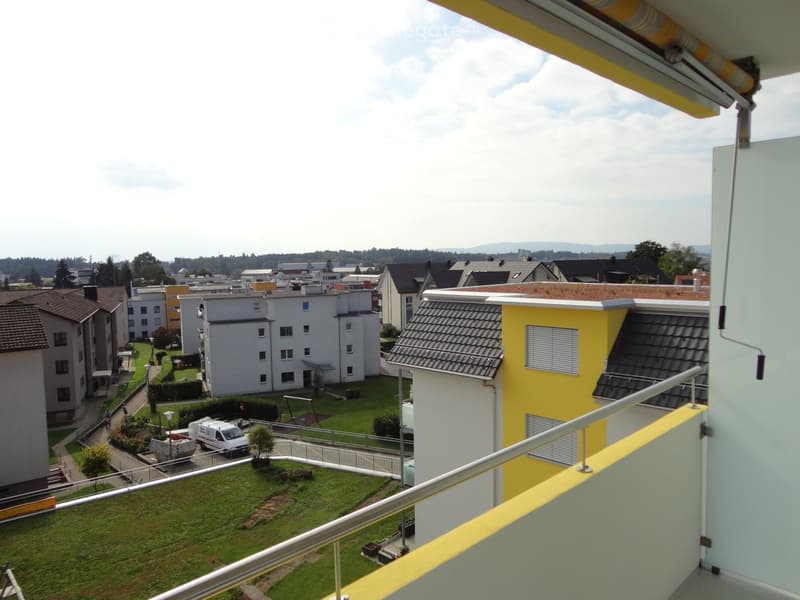Balcony overlooking a residential area with multiple buildings, green spaces, and a parking area.