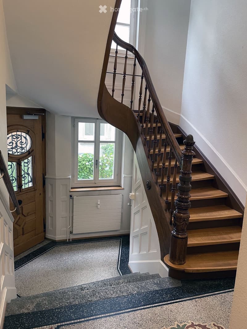 Spiral staircase with wooden steps and ornate balustrade, leading to a landing area with a window and door.