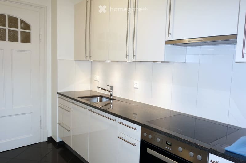 Modern kitchen with white cabinets, stainless steel appliances, and a black countertop.