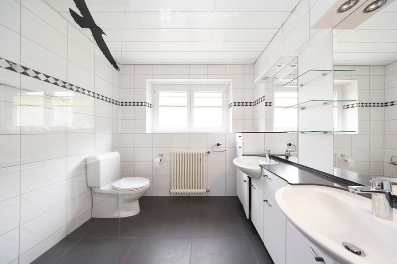 Modern bathroom with white tiles, a toilet, double sink, mirrored cabinet, and a radiator.