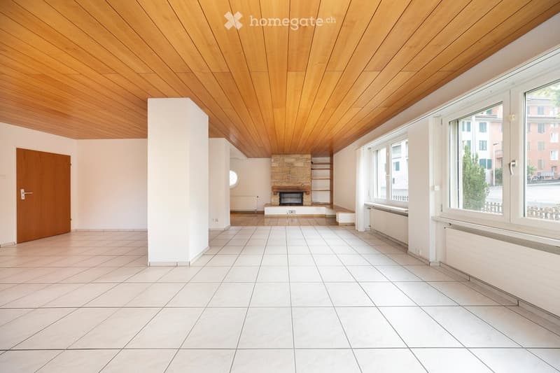 Empty living room with white tiled floor, wooden ceiling, large windows, and a stone fireplace.