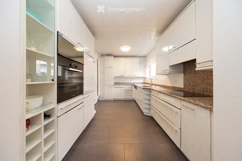 Modern kitchen with white cabinets, granite countertops, and stainless steel appliances including an oven and dishwasher. Shelves hold various items such as bowls and cups.