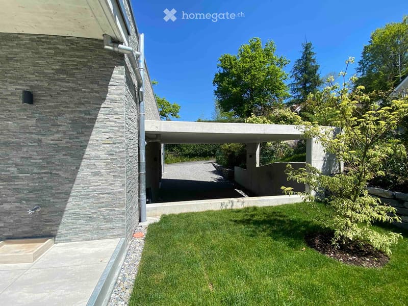 Modern house exterior with stone facade, covered walkway, and well-maintained lawn with trees.