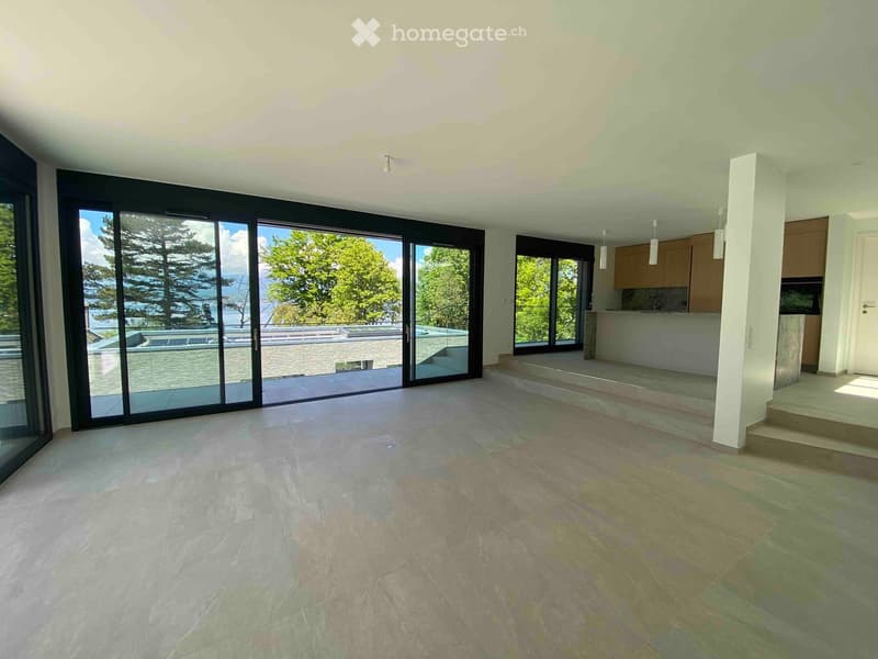 Open-plan space with large sliding glass doors leading to a balcony, tiled floor, and a small kitchen area with cabinets and a countertop visible in the background.