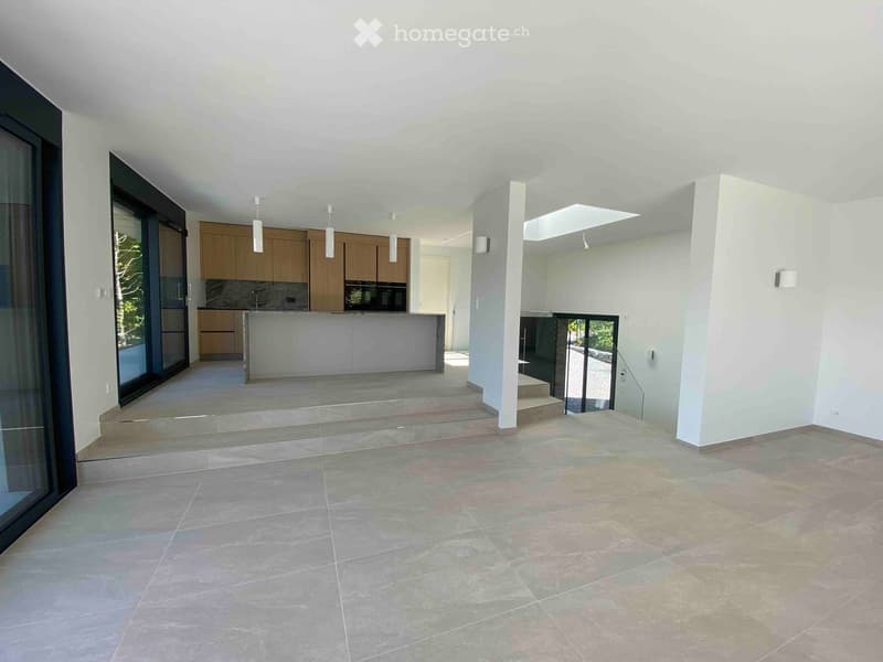 Open, modern space with tiled flooring, large glass windows, and a raised kitchen area with wooden cabinets and a countertop.