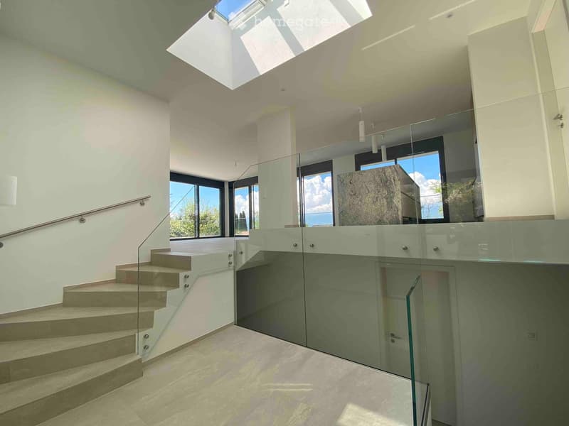 Modern interior staircase with glass railing, large windows, and skylight above.