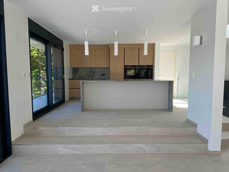 Modern kitchen with wooden cabinets, a central island, and a large window offering a view of greenery.