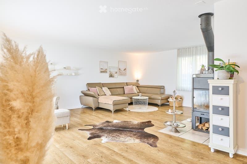 Modern living room with light-colored leather sofa, ottoman, coffee table, fireplace, and decorative elements.