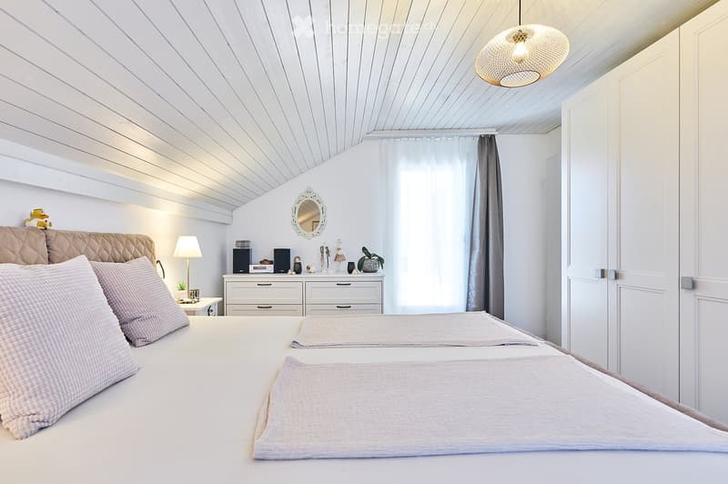 Cozy bedroom with a large bed, nightstand, lamp, mirror, and decorative items on a dresser.