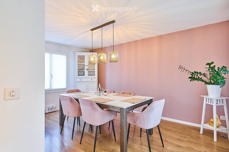 Dining room with a white dining table, pink upholstered chairs, pendant lights, a white cabinet, and a potted plant on a side table.
