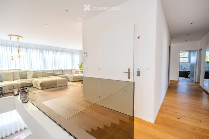 Living room with sofa, glass walls, wooden floor, hallway with staircase