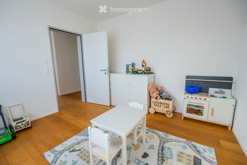 a playroom with a table, chairs, toy kitchen, storage boxes, toys, wooden floor, white walls