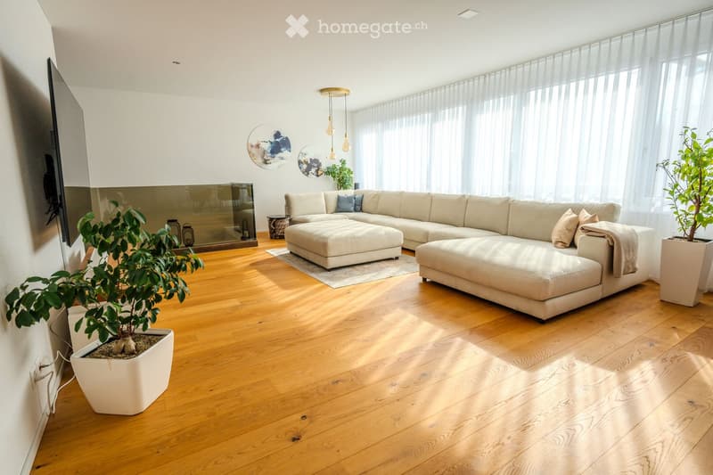 living room with modern beige sofa, wooden floor, white walls, mounted TV, white decorative plants, large windows with white curtains