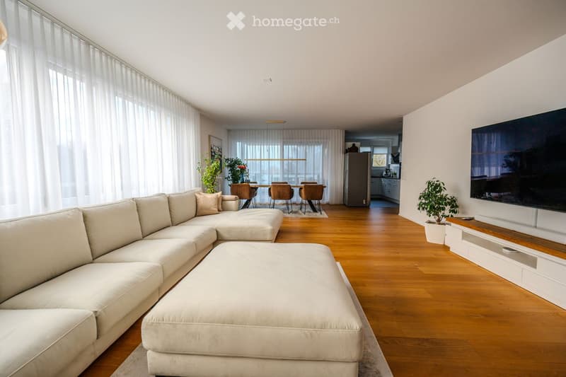 White couch, large windows with white curtains, large flat screen tv, wooden floor, plants