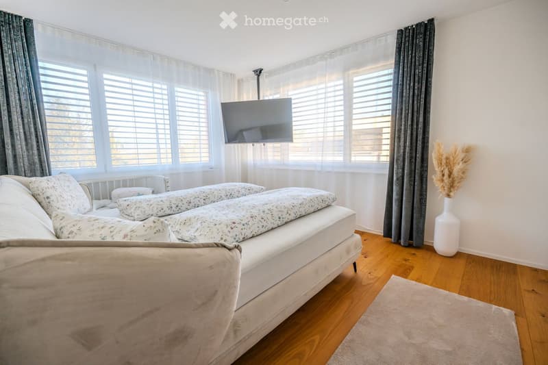 bedroom with double bed, two pillows, a small sofa, a TV, large window with curtains, carpet on floor