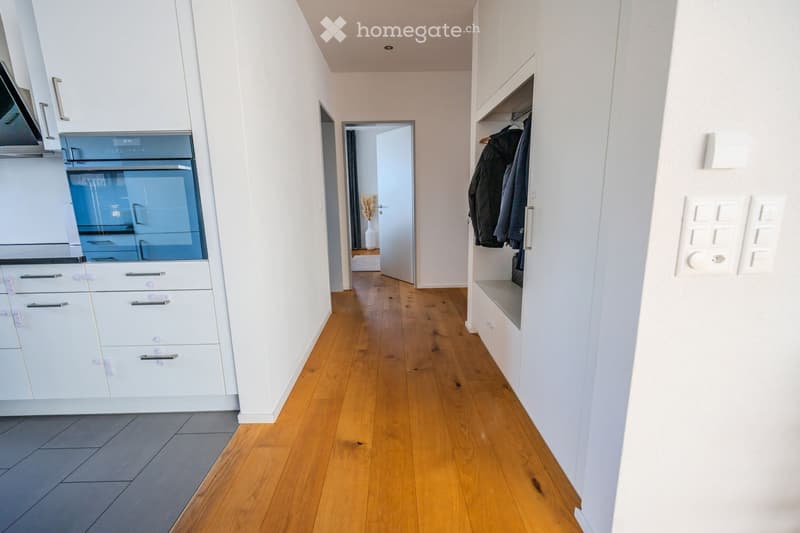 Wooden floor, white walls, kitchen with blue oven, hallway leading to room