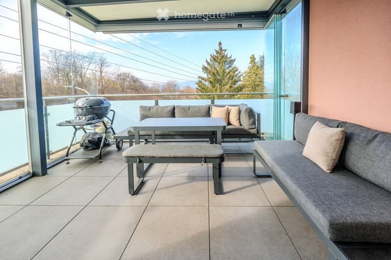 glass railing, grey couch, coffee table, bbq, tile floor, trees view
