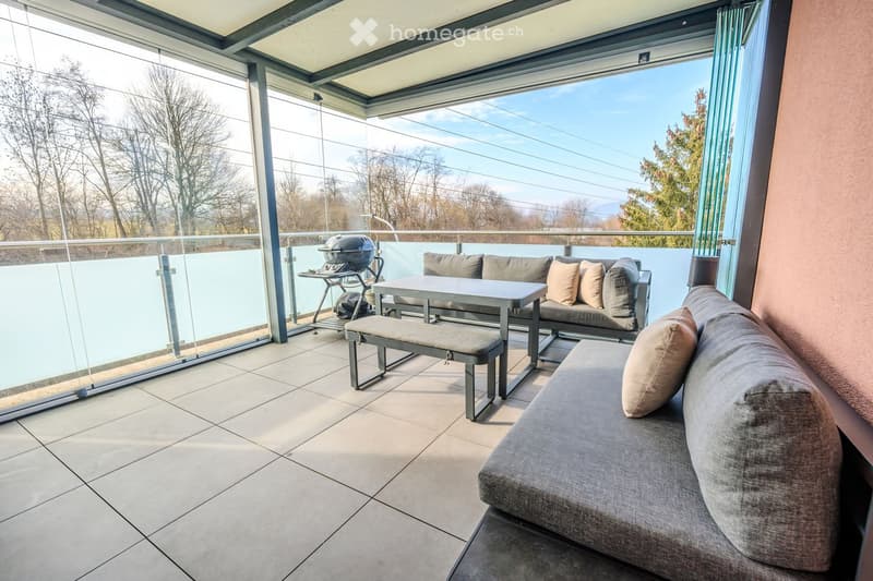 glass railings, grey lounge area, table, griller, pine trees, mountains, clear sky