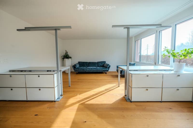 A room with a blue sofa, white cabinets, hardwood floors, and large windows providing a view outside.