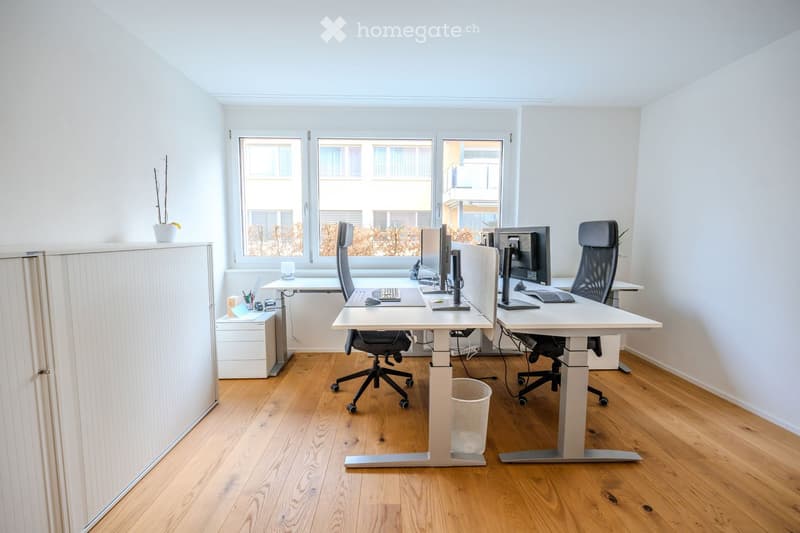 two desks, two chairs, trash bin, large window, wooden floor