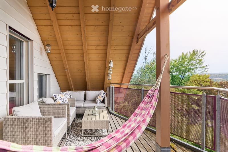 Wooden balcony with a scenic view, featuring a sofa, table, wicker chair, and hammock.