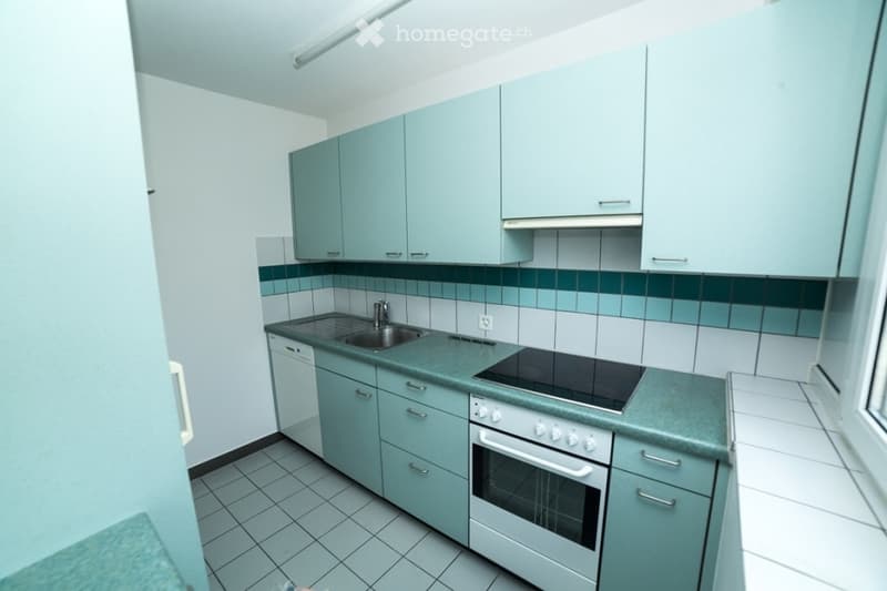 Modern kitchen with light blue cabinets, white tiles, and stainless steel appliances including a sink, oven, and dishwasher.