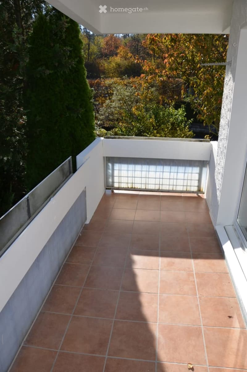 Balcony with tiled floor, white railings, and a view of trees and greenery.