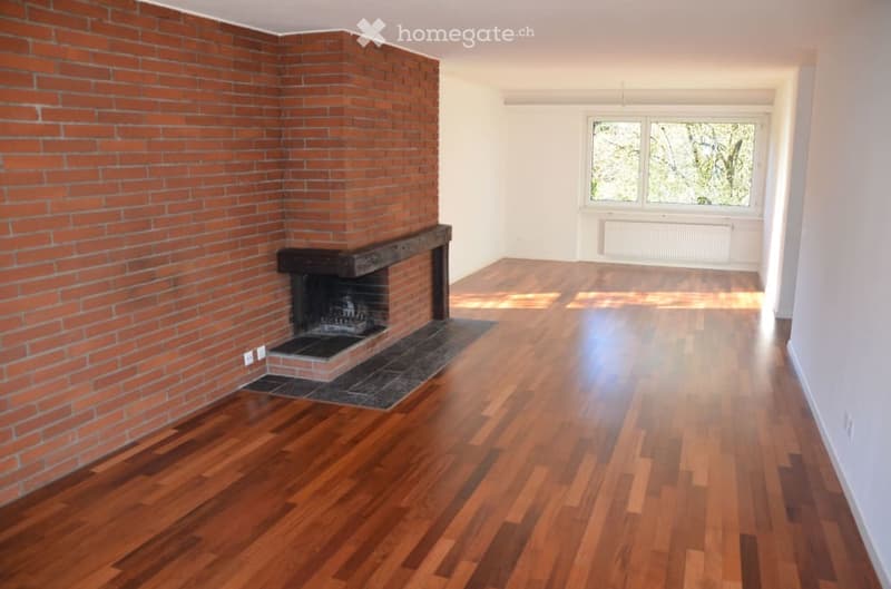 Empty room with wooden flooring, brick wall, and fireplace. No furniture or equipment present.