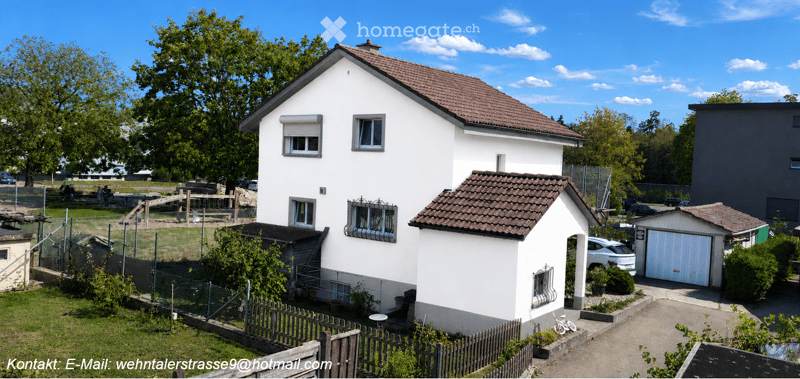 Two-story white house with red-tiled roof, multiple windows, garage, and fenced yard with greenery.