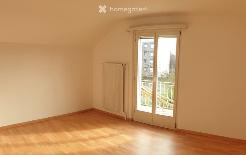 Empty room with wooden flooring, white walls, a radiator, and a large sliding glass door leading to a balcony or outdoor area.