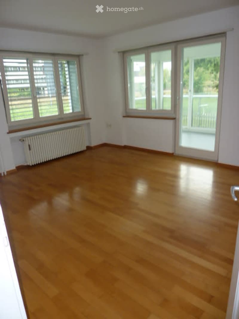 Empty room with wooden flooring, large windows, radiators, and access to a balcony.
