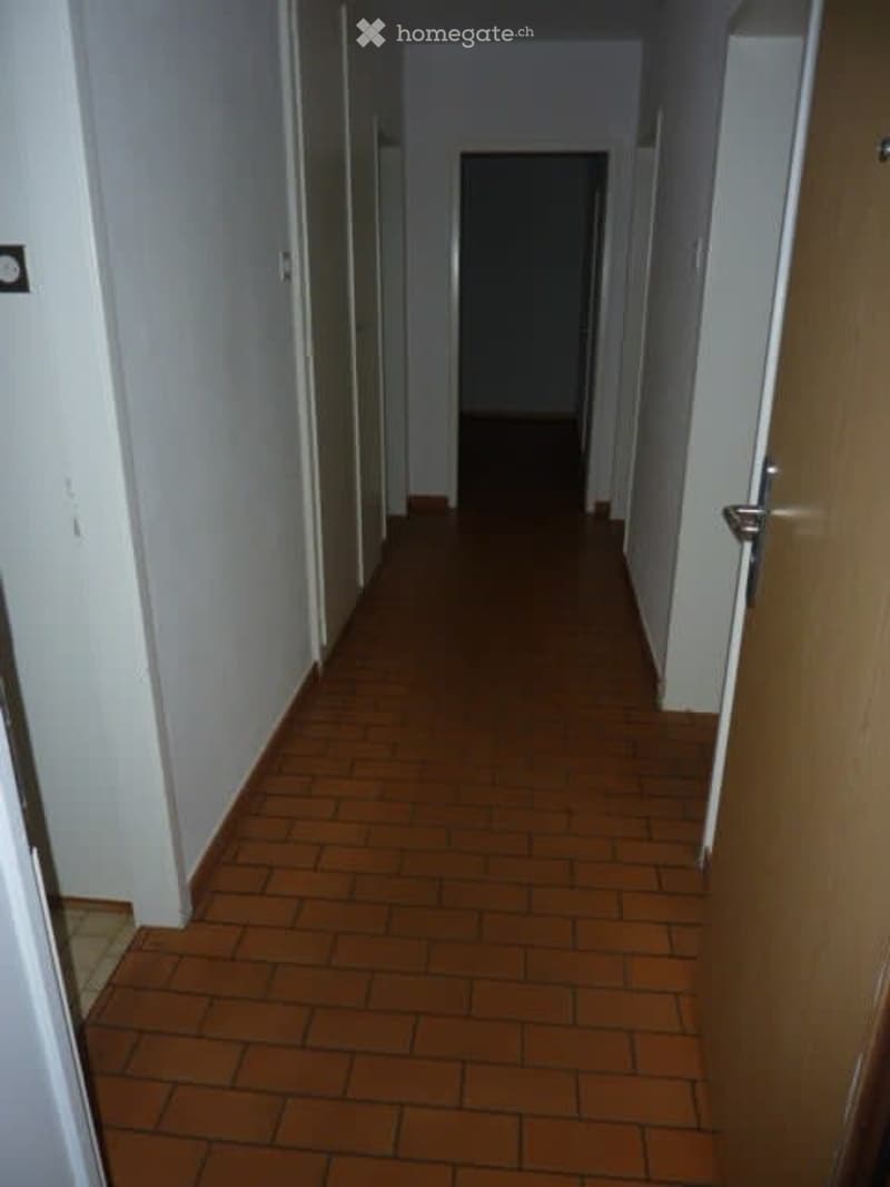 Empty hallway with wooden doors on both sides and a tiled floor.