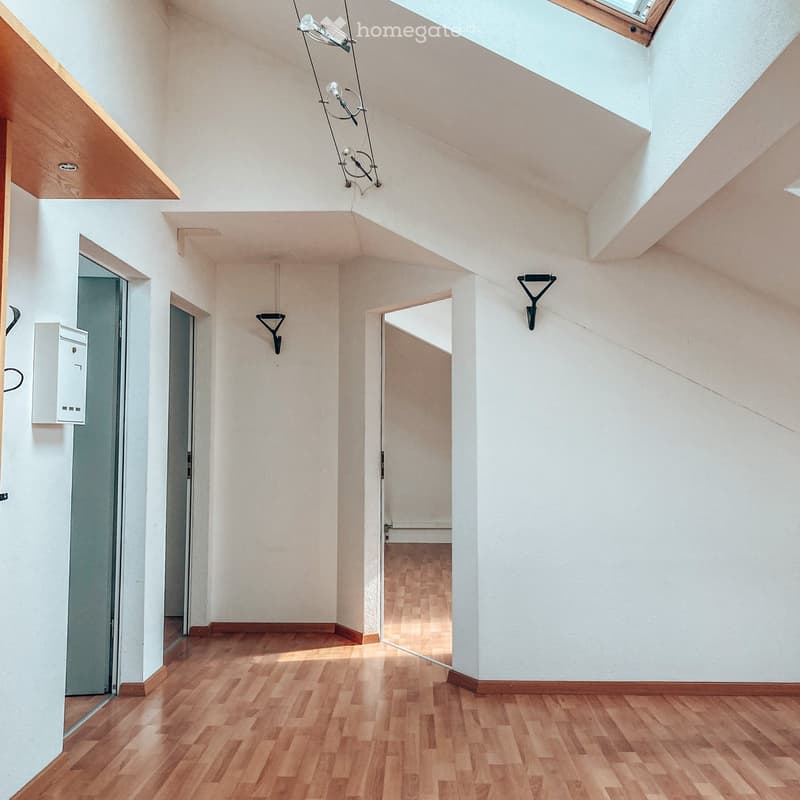 Empty hallway with wooden flooring, white walls, and several doors leading to other rooms. The ceiling has exposed beams and a skylight.