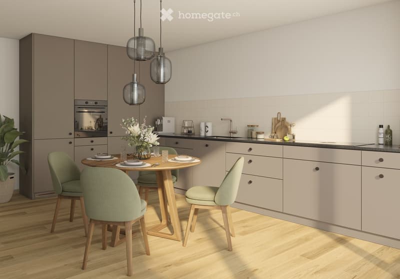 Modern kitchen with light-colored cabinets, a round wooden dining table with four green chairs, a vase with white flowers, and various kitchen items on the counter.