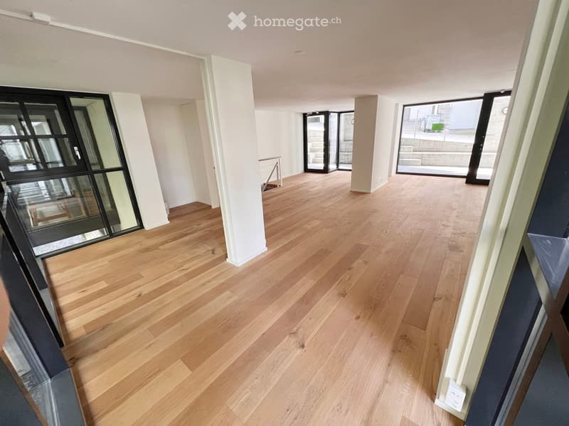 Empty hallway with light wooden flooring, white walls, and large glass doors leading outside.