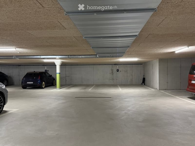 Underground parking area with concrete floors and walls, several parked cars, and a central support column.