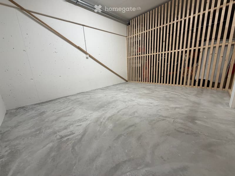 Empty room with concrete floor and white walls, featuring a wooden partition and exposed pipes.
