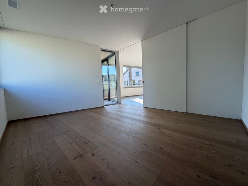Empty room with wooden flooring and white walls, featuring a large sliding glass door leading to a balcony.