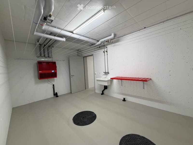 Minimalist bathroom with white walls, concrete floor, a single sink, red shelf, and a red electrical panel on the wall.