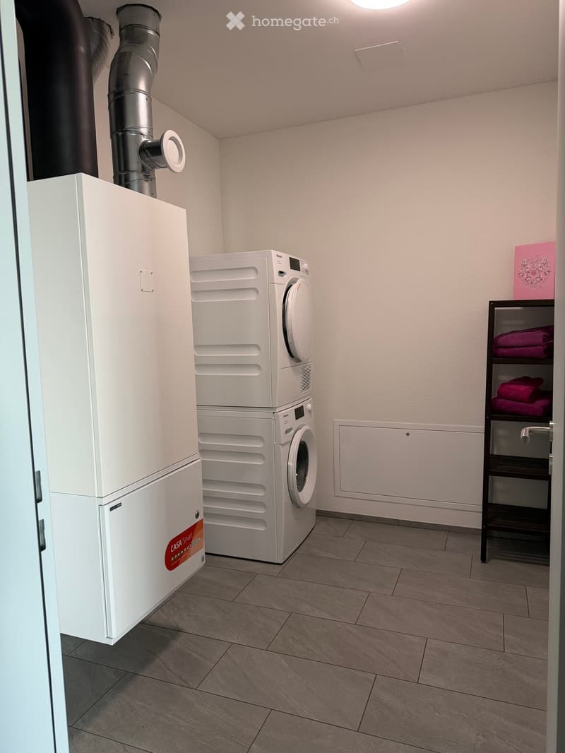 Modern bathroom with a white washing machine, a towel rack with pink towels, and a white water heater unit.